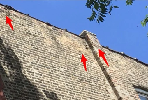 Cracked coping and spalling brick on a rooftop parapet wall
